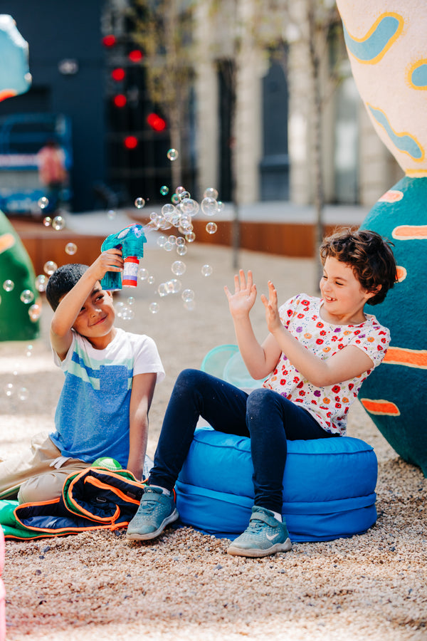 Two children sitting on a storage pouf playing outdoors with bubbles